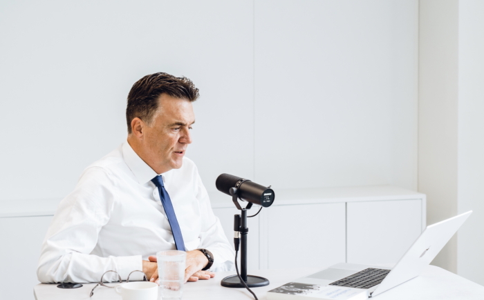 een man zit voor een microfoon en maakt dankzij 50 Koffies Producties een podcast