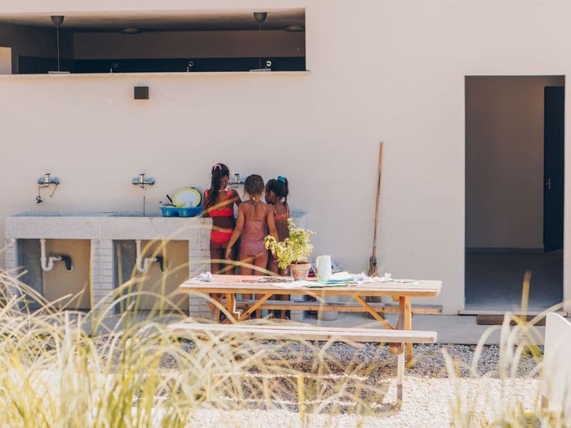 Kinderen doen samen de afwas bij de buitenafwasplaats van Camping Vista Fermo, met een picknicktafel op de voorgrond