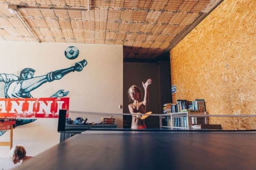 Kind speelt tafeltennis in de recreatieruimte van Camping Vista Fermo, met een voetbalmuurschildering en een kast vol boeken