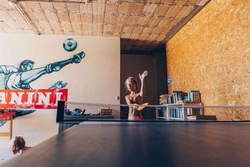 Tafeltennissen in de recreatieruimte van Camping Vista Fermo Kind speelt tafeltennis in de recreatieruimte van Camping Vista Fermo, met een voetbalmuurschildering en een kast vol boeken
