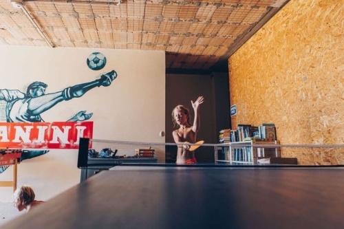 Kind speelt tafeltennis in de recreatieruimte van Camping Vista Fermo, met een voetbalmuurschildering en een kast vol boeken