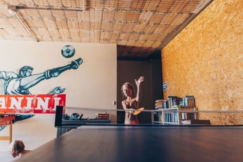 Kind speelt tafeltennis in de recreatieruimte van Camping Vista Fermo, met een voetbalmuurschildering en een kast vol boeken