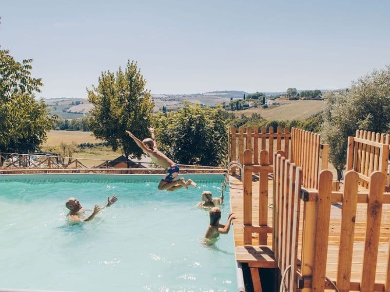 Spelende kinderen in het zwembad van Camping Vista Fermo, met uitzicht over de heuvels van Le Marche