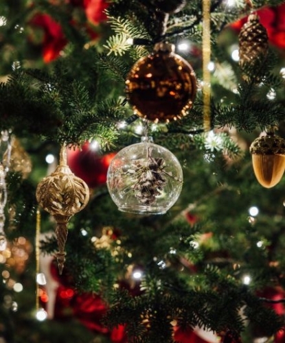 Kerstboom met gouden kerstballen, een glazen bal met dennenappel en twinkelende lichtjes