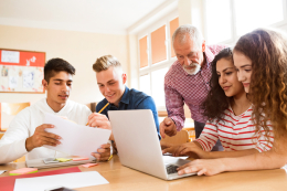 Leerlingen en docent bekijken profielwerkstukmodule achter laptop.