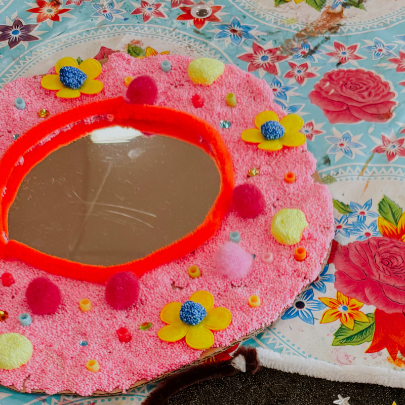 Spiegeltjes versieren workshop — van nachthemel tot bloemenpracht Twee versierde spiegeltjes — een zwarte nachthemel met sterren en vallende ster naast een roze spiegel met bloemen en pompons
