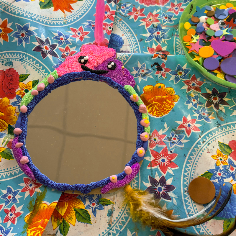 Spiegeltje met foamklei-monstertje en veertje Blauw-paars spiegeltje met een roze foamklei-monstertje bovenop met wiebeloogjes en een roze veertje