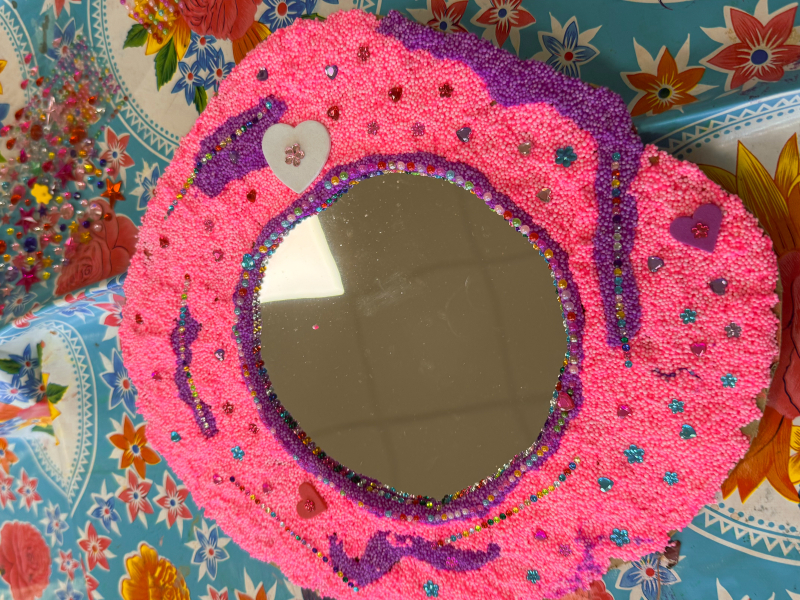 Rond spiegeltje versierd met roze en paarse foamklei, strass-steentjes en hartjes — resultaat van de spiegeltjes versieren workshop