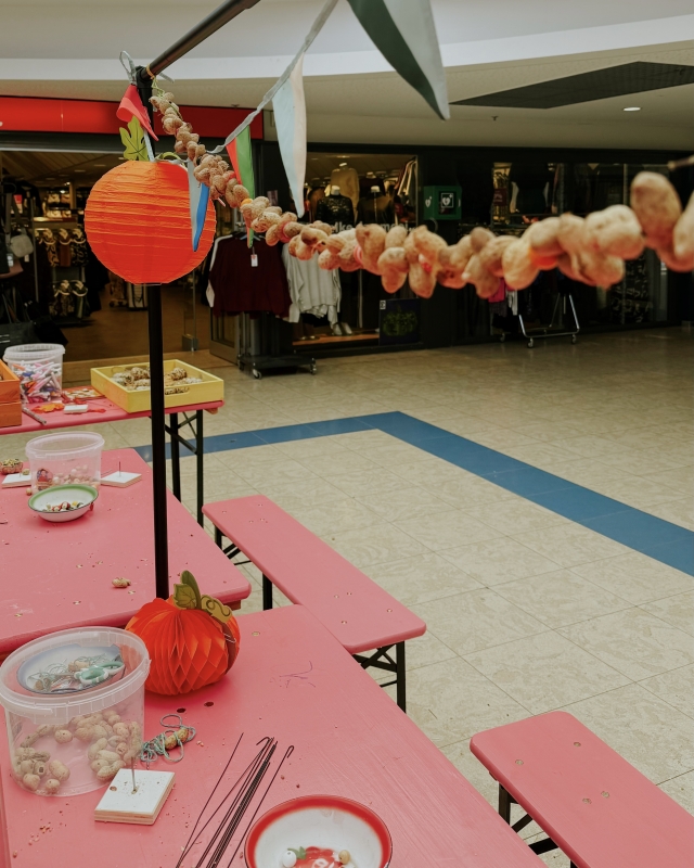 Herfstgedecoorde eventruimte in winkelcentrum met roze tafels, rode papieren pompoenen en peanut garland slingers als decoratie