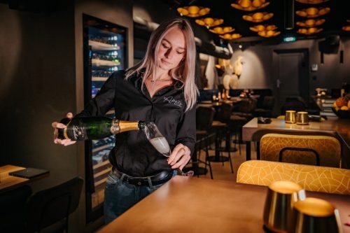Medewerkster schenkt champagne in aan de bar van Apéro by Luigi's in Harderwijk