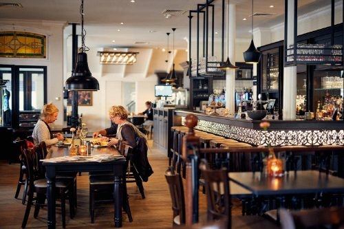 Brasserie De Lindeboom op Texel Lange houten tafels, een verlichte bar en zwarte hanglampen in de brasserie van De Lindeboom in Den Burg op Texel