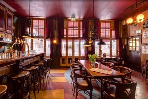 Bruin café met lange bar, houten tafels en hoge ramen in Café De Kartouwe in Doetinchem