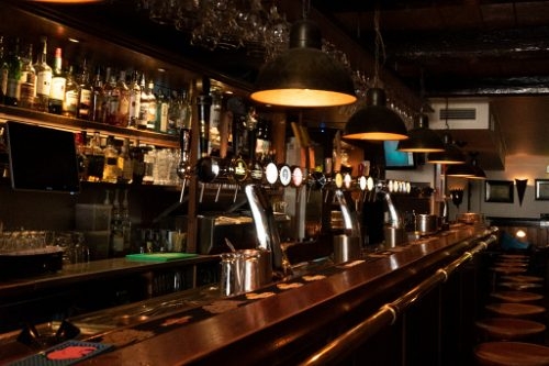 Lange houten bar met biertaps, hanglampen en een wand vol flessen in café Camelot in Zutphen