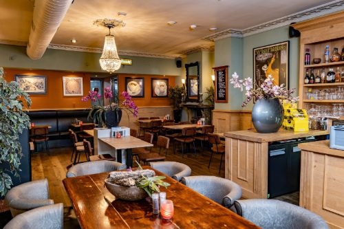 Interieur van De Graaf van Gelre met lange houten tafel, grijze stoelen en een kroonluchter in Harderwijk