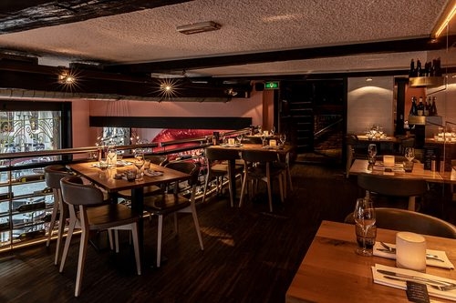 Eetzaal van Jackies NYC met houten tafels, grijze stoelen en een raam met goudkleurig sierhekwerk in Deventer