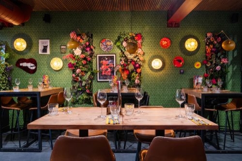 Gedekte tafels voor een groene wand met bloemen en ronde lampen bij KB Food & Drinks in Dokkum