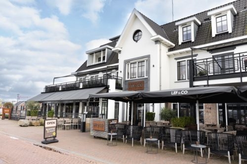 Witte gevel van Lef & Co met terras en zwarte parasols aan de Strandboulevard in Harderwijk