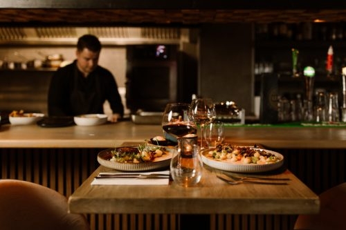 Open keuken met een chef achter de bar en een gedekte tafel met gerechten in Leo's Kitchen & Bar in Lelystad