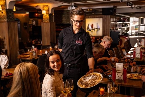Ober serveert een pannenkoek aan een tafel vol gasten in restaurant Lotje aan de haven van Volendam