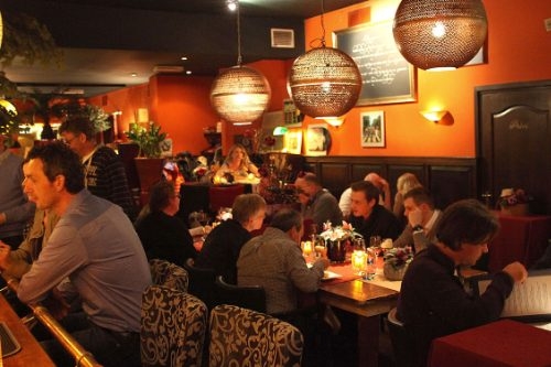 Volle restaurantzaal met oranje muren en ronde hanglampen in Eterij & Tapperij 't Raedthuys in Doetinchem