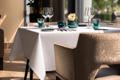 Gedekte tafel met wit tafelkleed, wijnglazen en een bloemetje bij het raam in Restaurant Silver in Lelystad