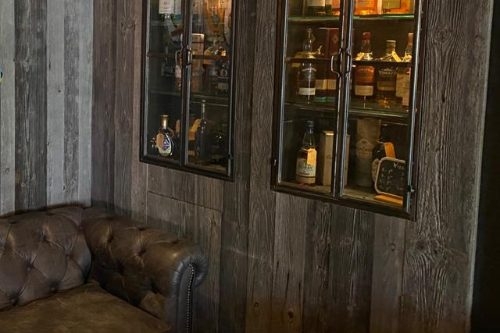 SoHo Gastrobar in Schagen Leren chesterfieldbank en twee verlichte whiskykasten tegen een houten wand in SoHo Gastrobar in Schagen