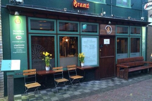 Taveerne De Twaalf Balcken op Texel Donkergroene gevel met houten klapstoeltjes en een bank voor de deur van Taveerne De Twaalf Balcken in Den Burg op Texel
