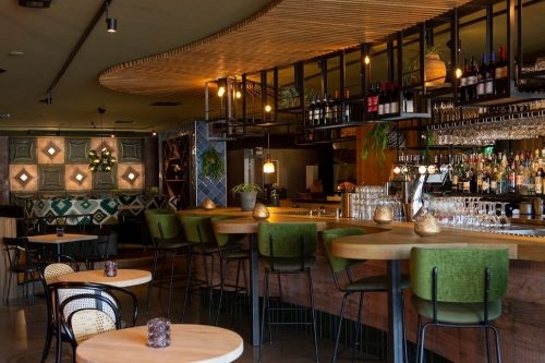 Wonder's in Schagen Lange houten bar met groene barkrukken en volle flessen- en glazenrekken in Wonder's in Schagen