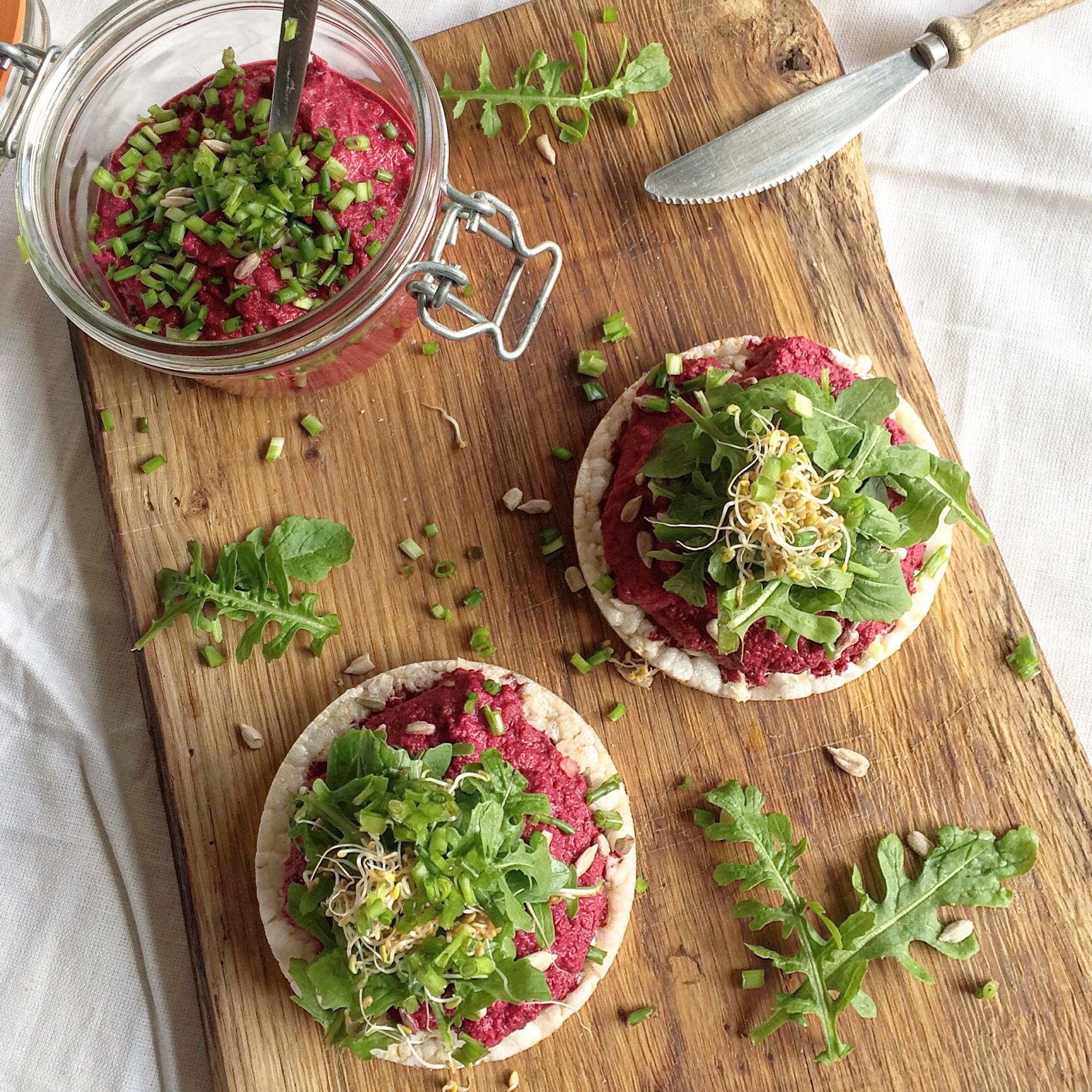 Een flinke laag bietenspread, rucola, bieslook op een rijstwafel.